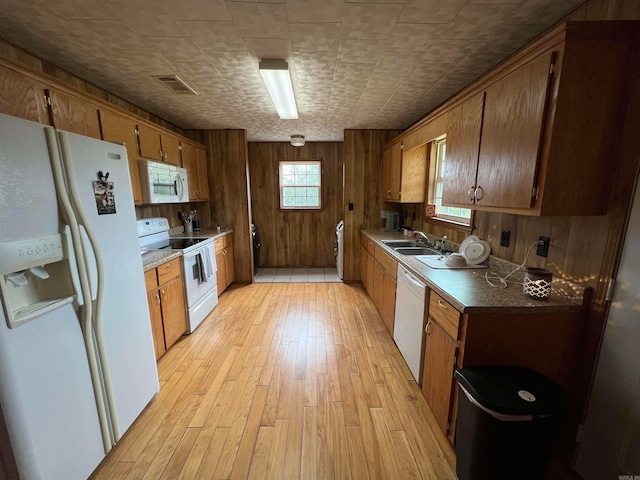 kitchen with washer / dryer, light hardwood / wood-style flooring, white appliances, sink, and wood walls