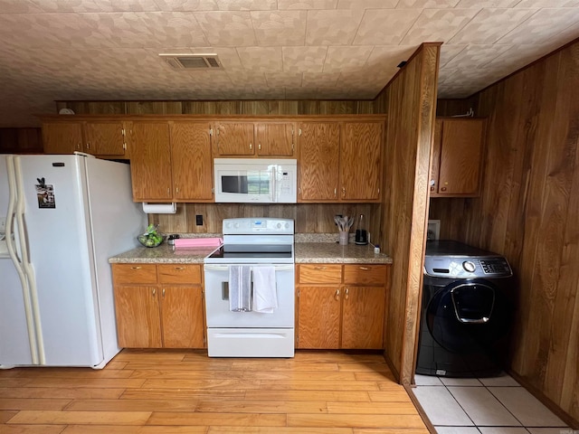 kitchen with light hardwood / wood-style floors, white appliances, wood walls, and washer / clothes dryer