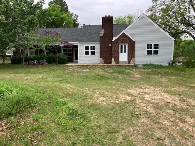 back of house with brick siding, a chimney, and a lawn