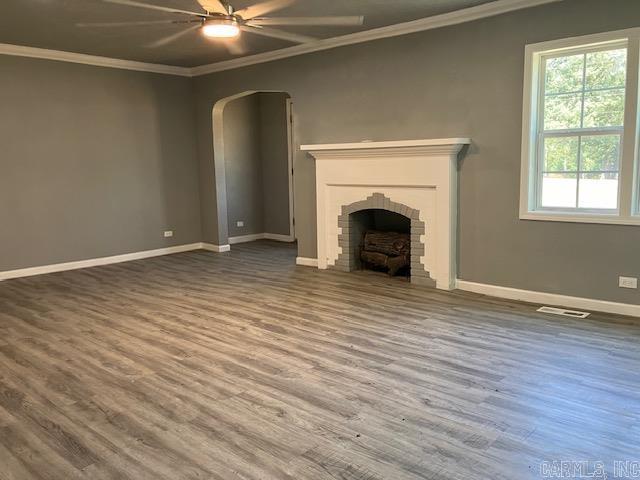 unfurnished living room featuring visible vents, arched walkways, wood finished floors, crown molding, and a fireplace