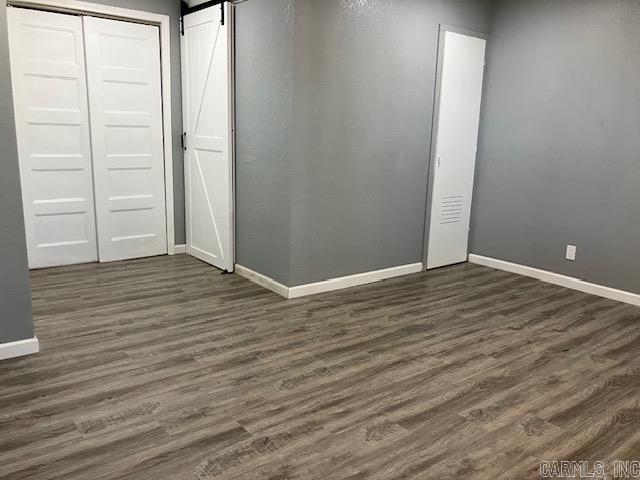 unfurnished bedroom featuring a barn door, baseboards, and dark wood finished floors