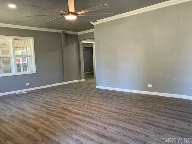 spare room featuring ornamental molding, dark wood-type flooring, a ceiling fan, and baseboards