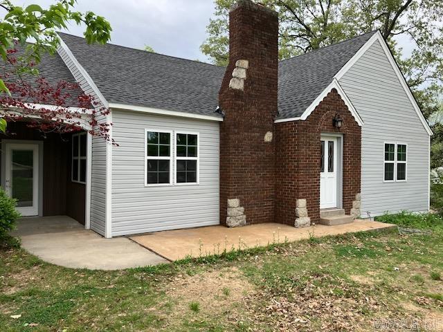 back of house featuring entry steps, a patio, roof with shingles, and a chimney