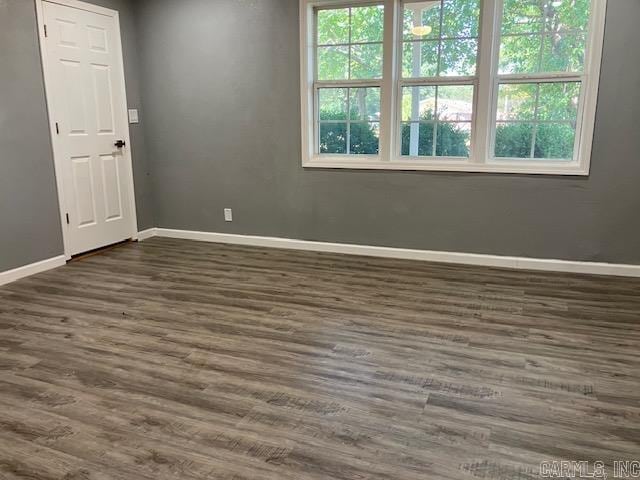 unfurnished room featuring dark wood-style flooring, a healthy amount of sunlight, and baseboards