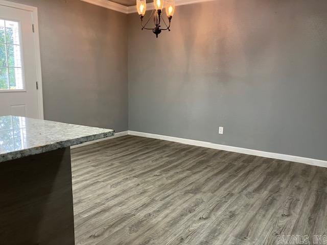 unfurnished dining area with dark wood-type flooring, a chandelier, ornamental molding, and baseboards