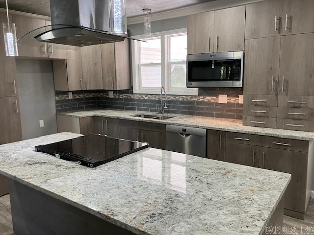 kitchen featuring light stone counters, stainless steel appliances, backsplash, a sink, and exhaust hood