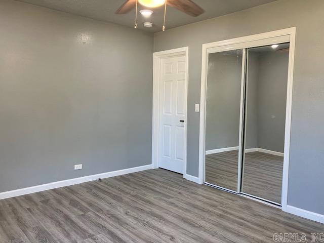 unfurnished bedroom featuring a ceiling fan, a closet, baseboards, and wood finished floors