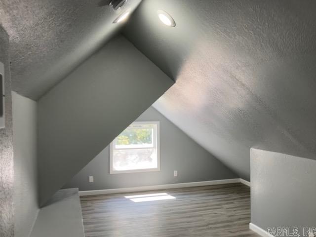 additional living space with a textured ceiling, vaulted ceiling, wood finished floors, and baseboards