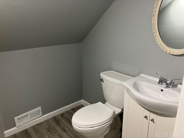 bathroom with lofted ceiling, toilet, wood finished floors, and visible vents