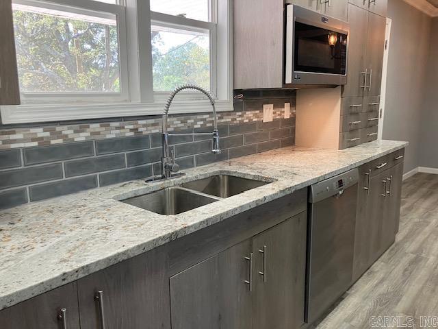 kitchen with appliances with stainless steel finishes, backsplash, a sink, and light wood-style flooring