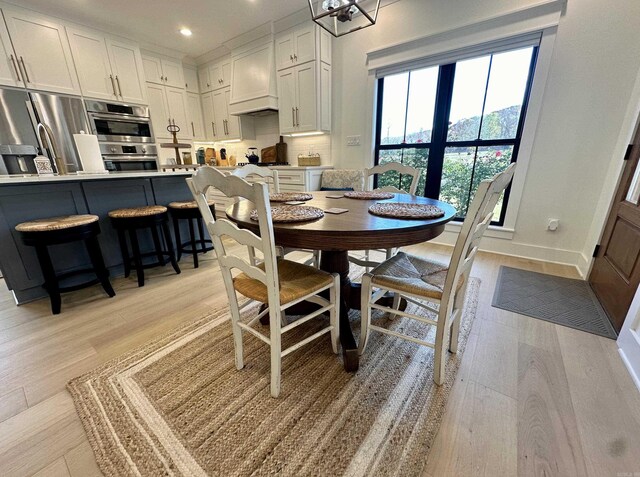 kitchen featuring light hardwood / wood-style floors, an island with sink, stainless steel appliances, a chandelier, and white cabinets