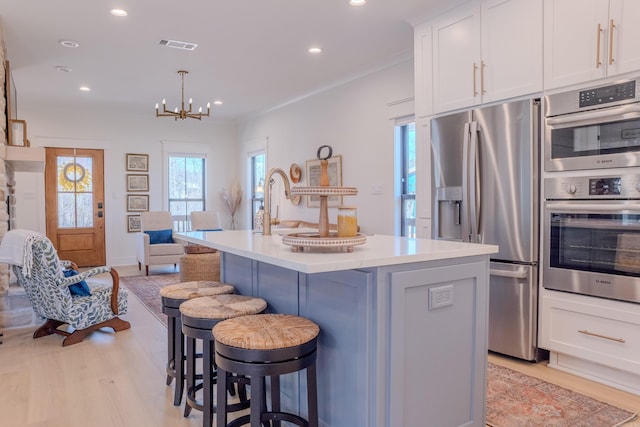 kitchen with white cabinets, hanging light fixtures, light hardwood / wood-style flooring, stainless steel appliances, and an island with sink