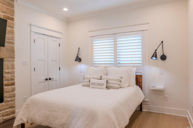 bedroom featuring a stone fireplace, ornamental molding, a closet, and light hardwood / wood-style floors