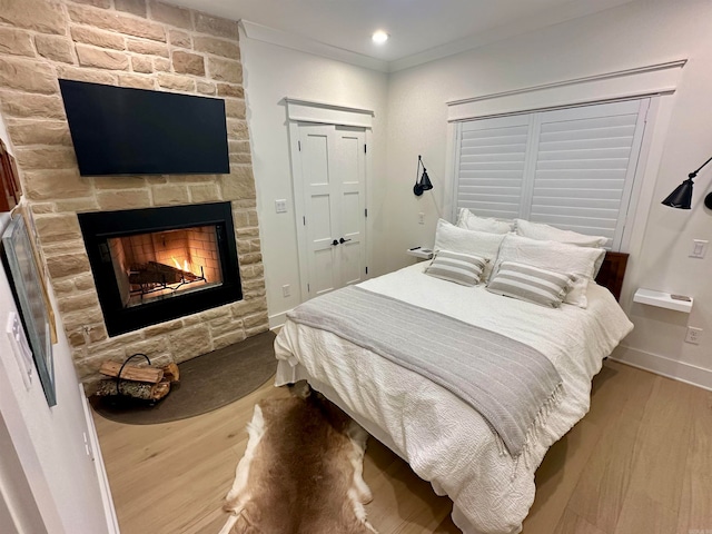 bedroom with light wood-type flooring, crown molding, and a stone fireplace