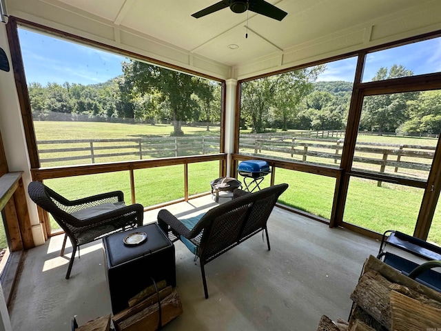 sunroom featuring ceiling fan and a rural view