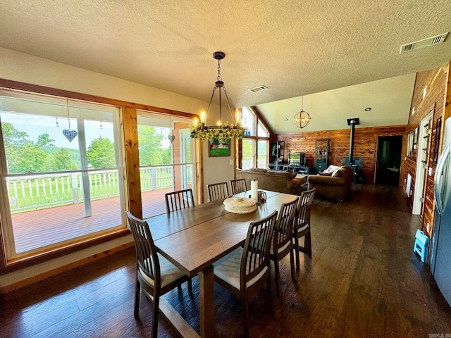 dining space with a notable chandelier, a textured ceiling, a wood stove, dark hardwood / wood-style flooring, and vaulted ceiling