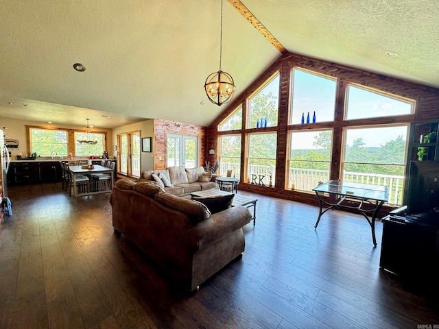 living room featuring a textured ceiling, an inviting chandelier, dark wood-type flooring, sink, and lofted ceiling