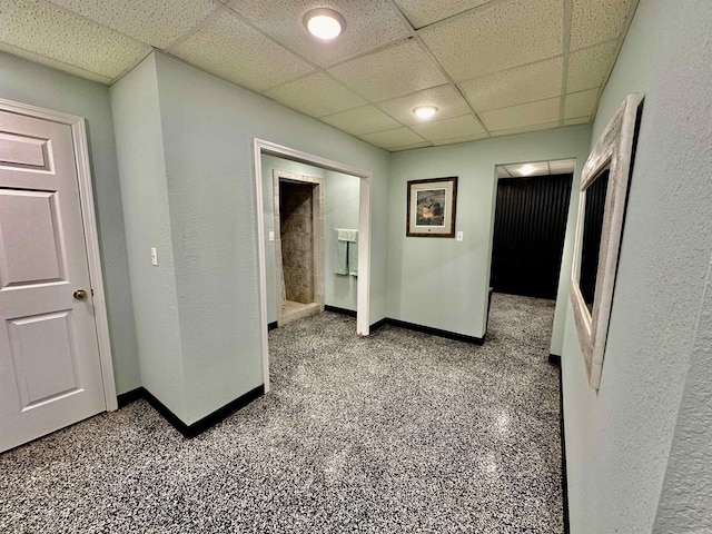 hall featuring a paneled ceiling, baseboards, and carpet