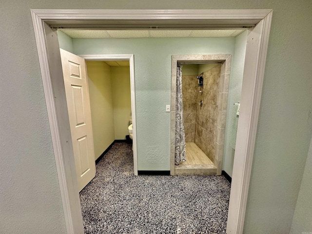 bathroom featuring baseboards, toilet, a shower stall, and a textured wall