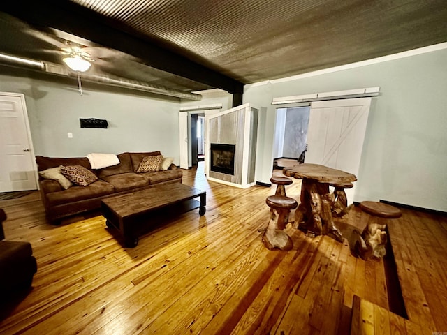 living area with a barn door, hardwood / wood-style flooring, a fireplace, and beam ceiling