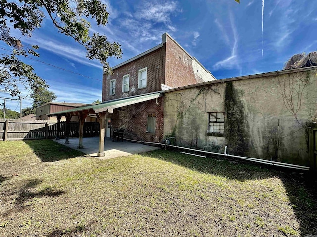 rear view of house with a yard, fence, brick siding, and a patio area