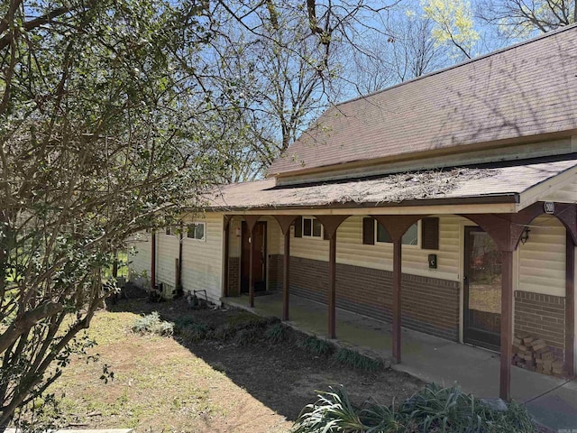 back of property featuring brick siding and roof with shingles
