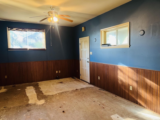 empty room featuring wooden walls, a wainscoted wall, and ceiling fan