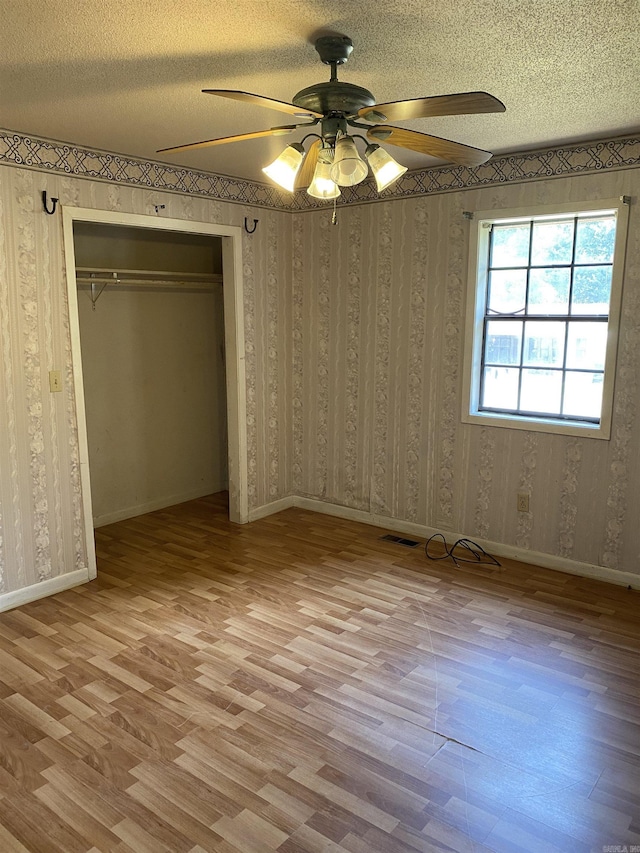 unfurnished bedroom with wallpapered walls, light wood-type flooring, and a textured ceiling