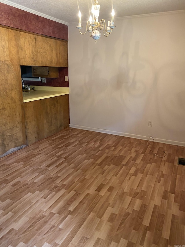 kitchen with a textured ceiling, wood finished floors, brown cabinetry, and ornamental molding