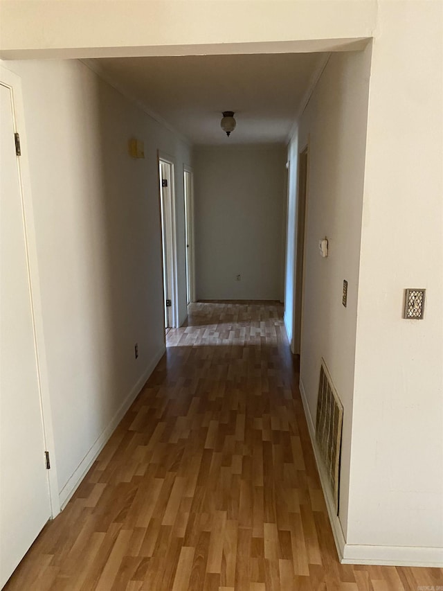 corridor with light wood-style floors, visible vents, and baseboards