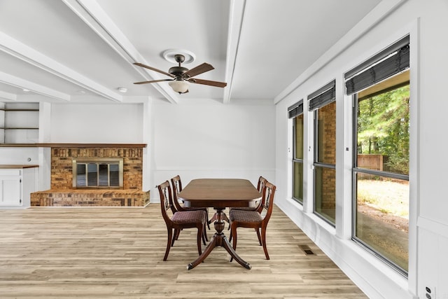 dining space featuring ceiling fan, beamed ceiling, light wood-type flooring, and a fireplace