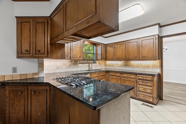 kitchen with dark stone counters, crown molding, stainless steel gas stovetop, kitchen peninsula, and sink