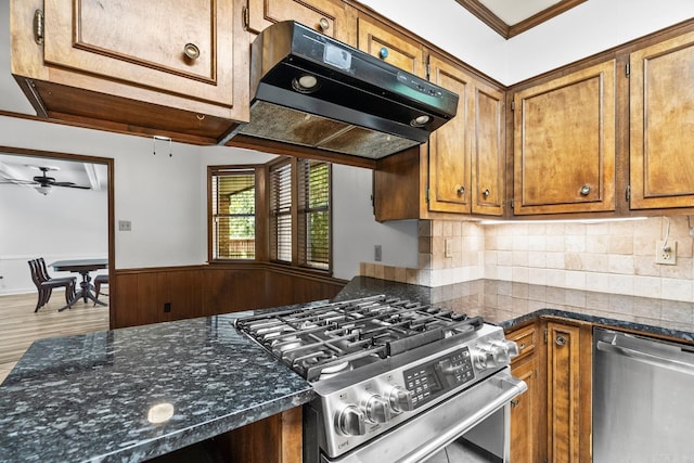 kitchen featuring hardwood / wood-style floors, crown molding, stainless steel appliances, ceiling fan, and dark stone counters