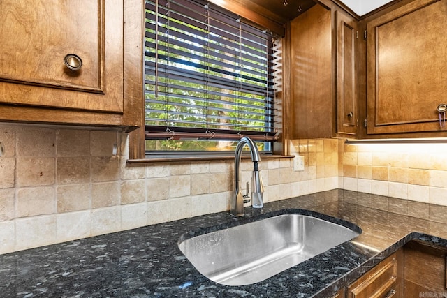 kitchen featuring backsplash, dark stone countertops, and sink