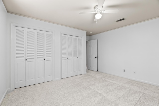 unfurnished bedroom featuring crown molding, ceiling fan, light carpet, and two closets