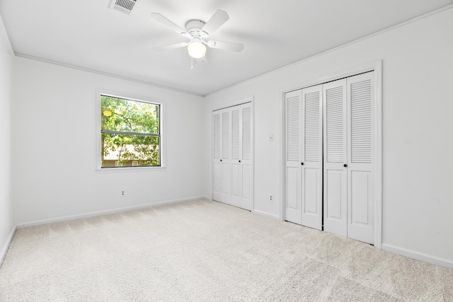 unfurnished bedroom featuring light colored carpet, ceiling fan, ornamental molding, and multiple closets