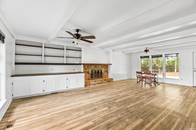 unfurnished living room featuring light wood-type flooring, ceiling fan, beamed ceiling, and a brick fireplace