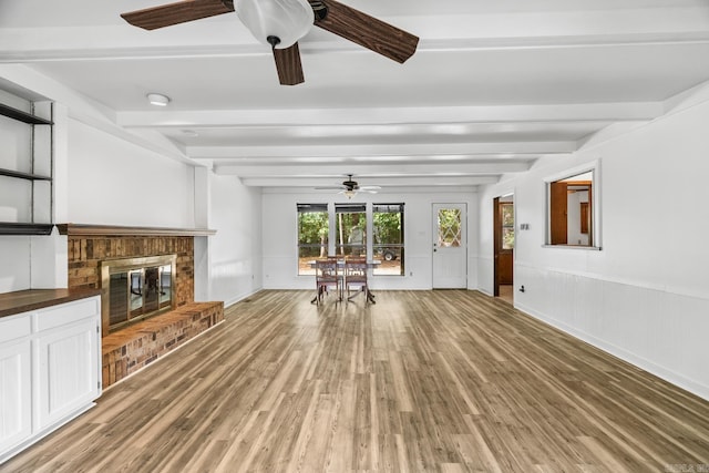 unfurnished living room with ceiling fan, hardwood / wood-style flooring, a fireplace, and beam ceiling