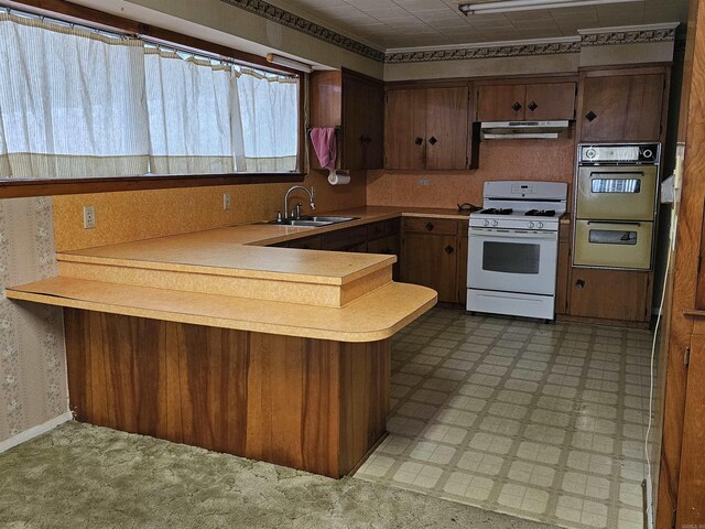 kitchen with stainless steel double oven, kitchen peninsula, sink, a breakfast bar area, and white gas range