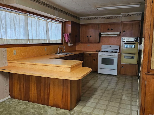 kitchen with double oven, white gas range, kitchen peninsula, and sink