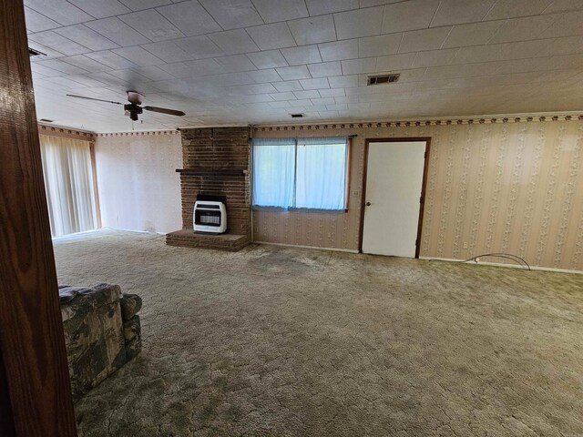 empty room with a wood stove, a brick fireplace, heating unit, ceiling fan, and carpet floors