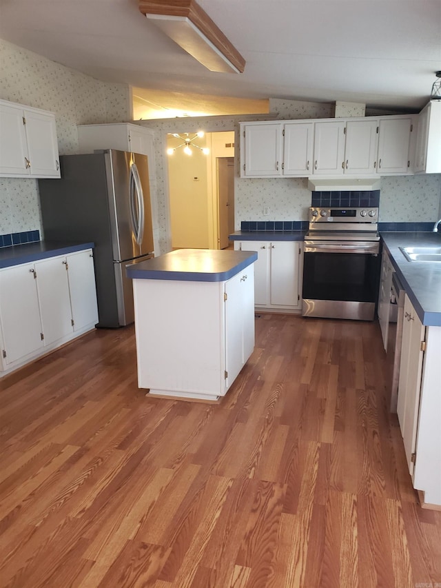 kitchen featuring appliances with stainless steel finishes, white cabinetry, wood-type flooring, and vaulted ceiling