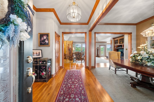 entrance foyer with light wood-type flooring, ornamental molding, and an inviting chandelier