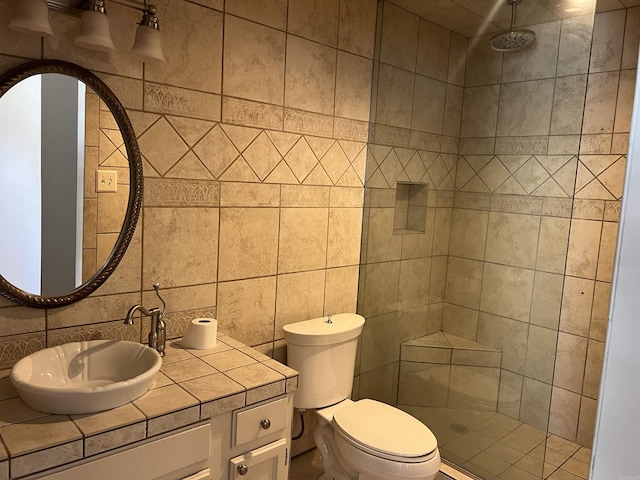 bathroom with a tile shower, tile walls, vanity, and toilet