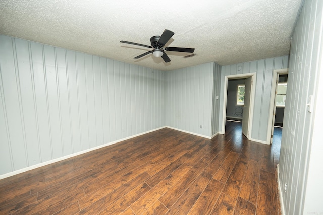 unfurnished room featuring wood walls, ceiling fan, dark hardwood / wood-style floors, and a textured ceiling