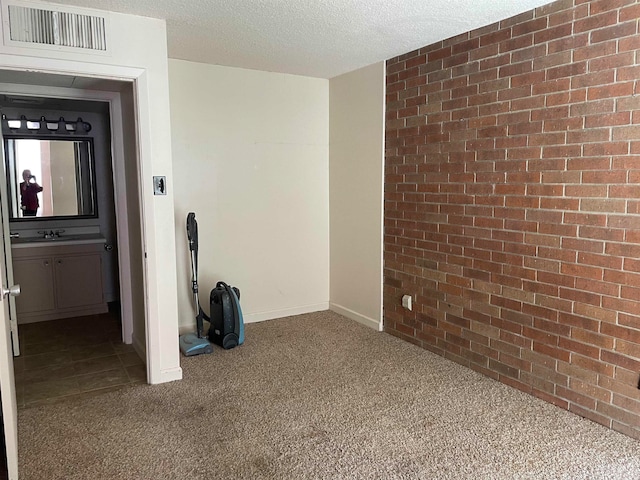 unfurnished room with sink, carpet floors, brick wall, and a textured ceiling