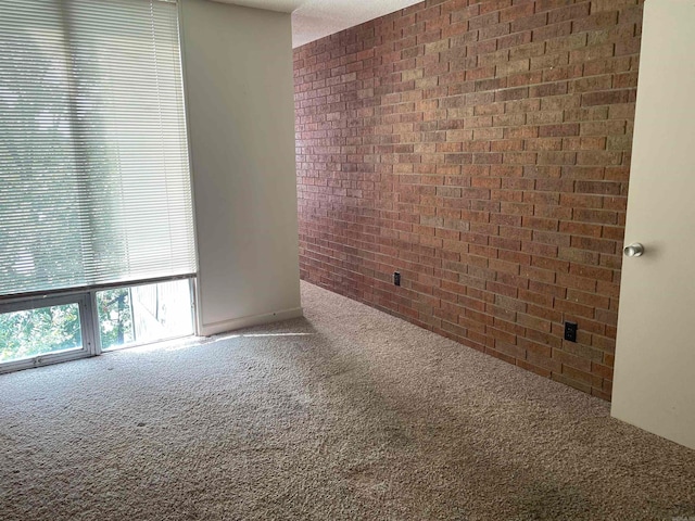 carpeted empty room featuring brick wall