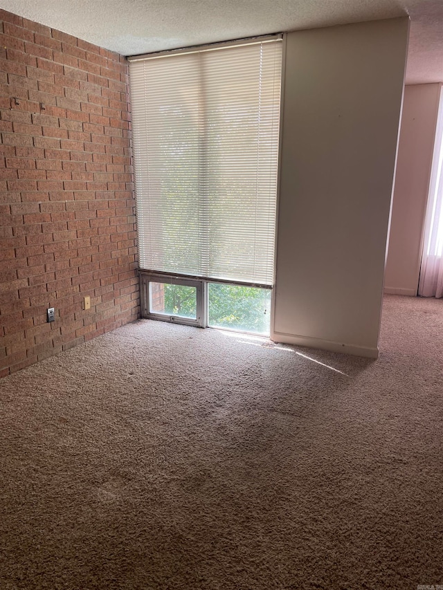 carpeted spare room with a textured ceiling and brick wall