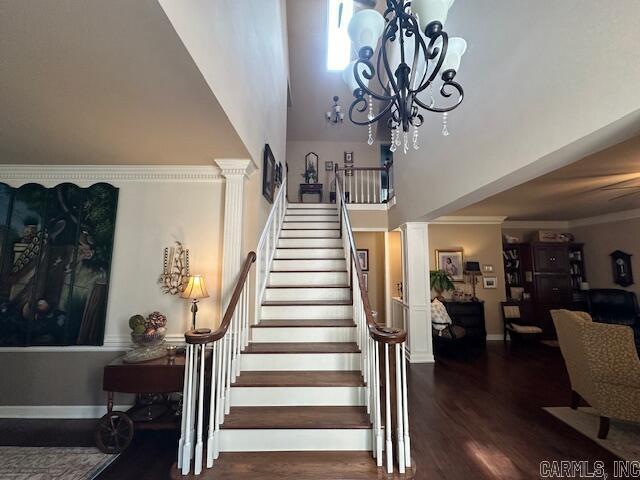 stairs featuring crown molding, decorative columns, an inviting chandelier, wood finished floors, and a towering ceiling