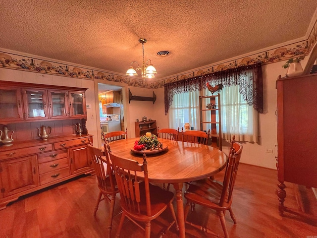 dining room with wood finished floors, visible vents, ornamental molding, a textured ceiling, and a chandelier